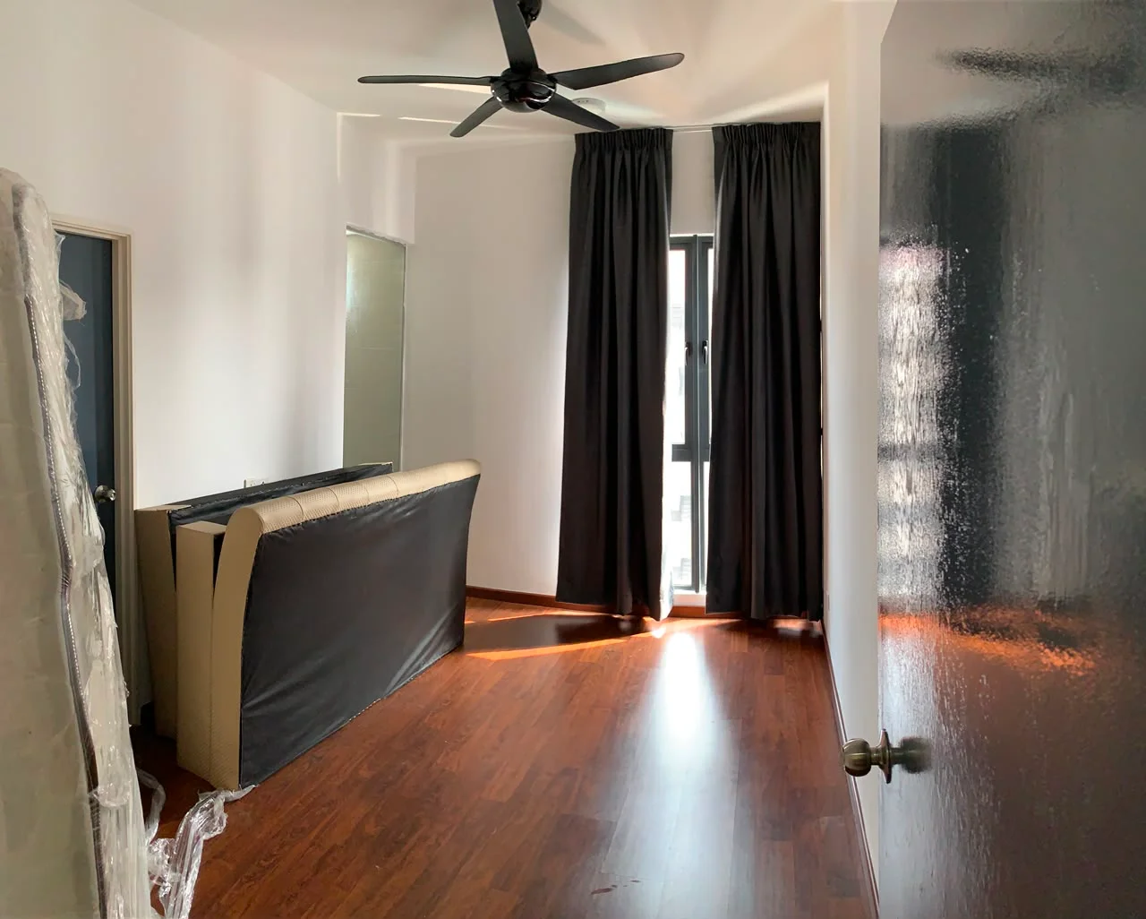Room features: wooden flooring, white painted walls, blackout curtains, 5-blade ceiling fan, floor-to-ceiling window, sofa, door, natural light; style: modern.